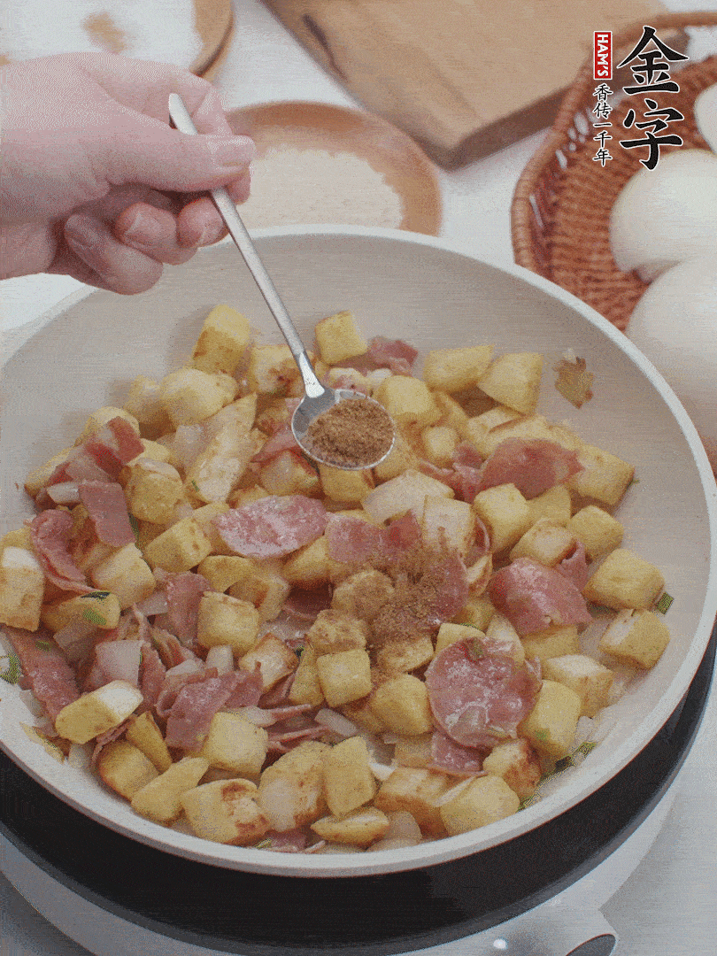 起鍋少油，煸香洋蔥丁、蔥白，加入金字培根火腿翻炒幾下，再加入饅頭丁、1小勺孜然粉、少許鹽翻炒均勻并鋪平。